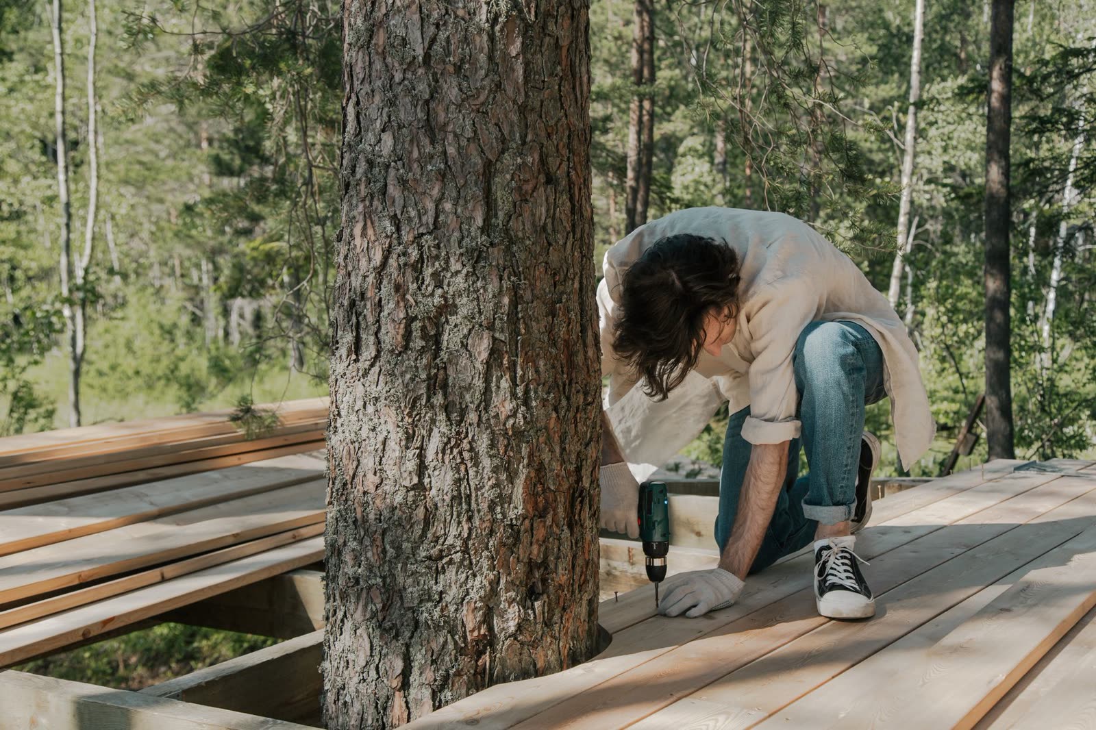 Worker drilling wooden boardwalk on a forested shoreline